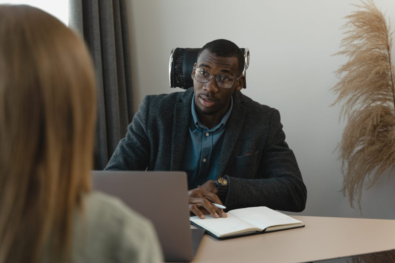 A man wearing glasses and holding a laptop is looking straight ahead